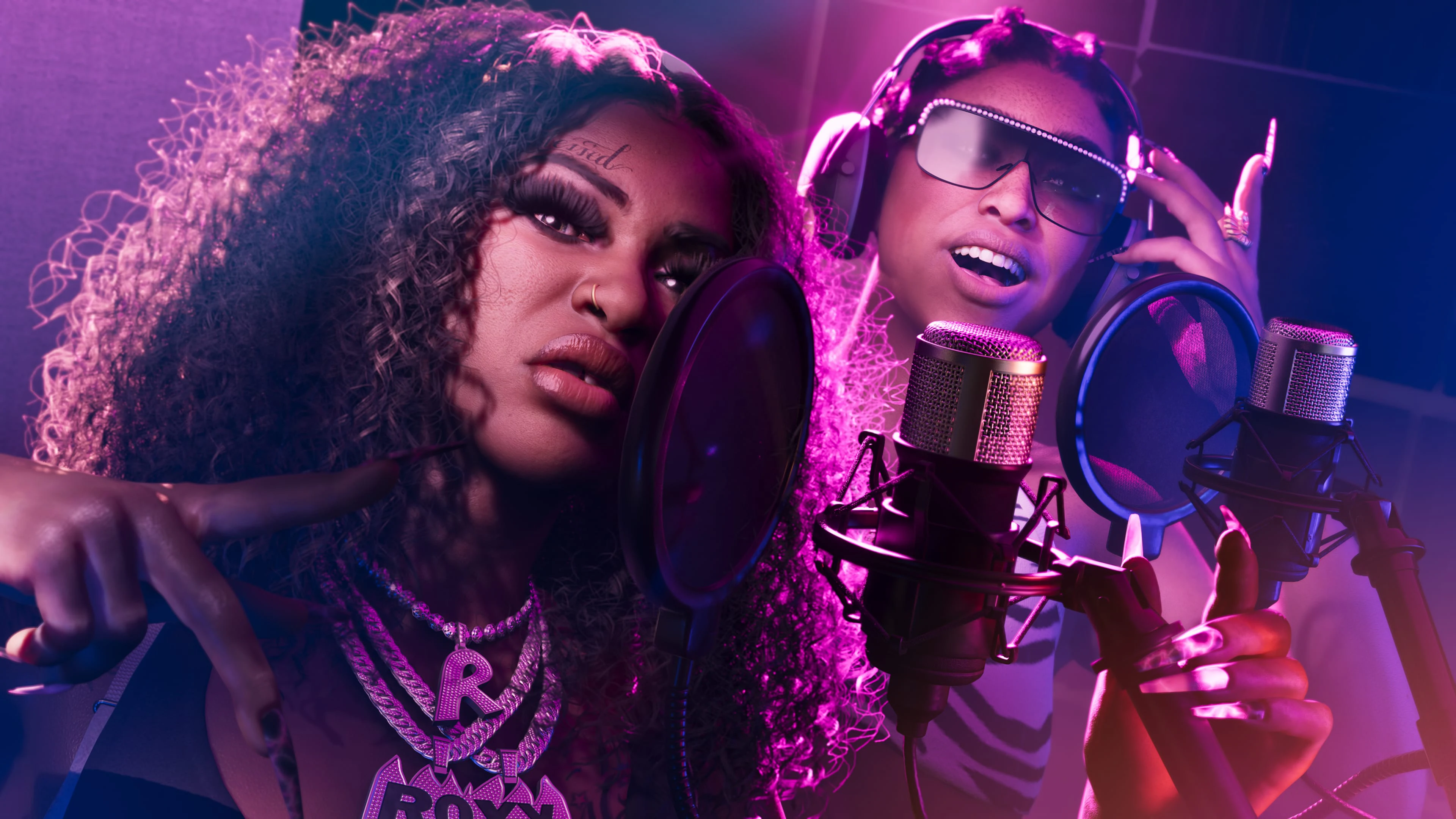 Two adult recording artists performing into studio microphones under magenta light