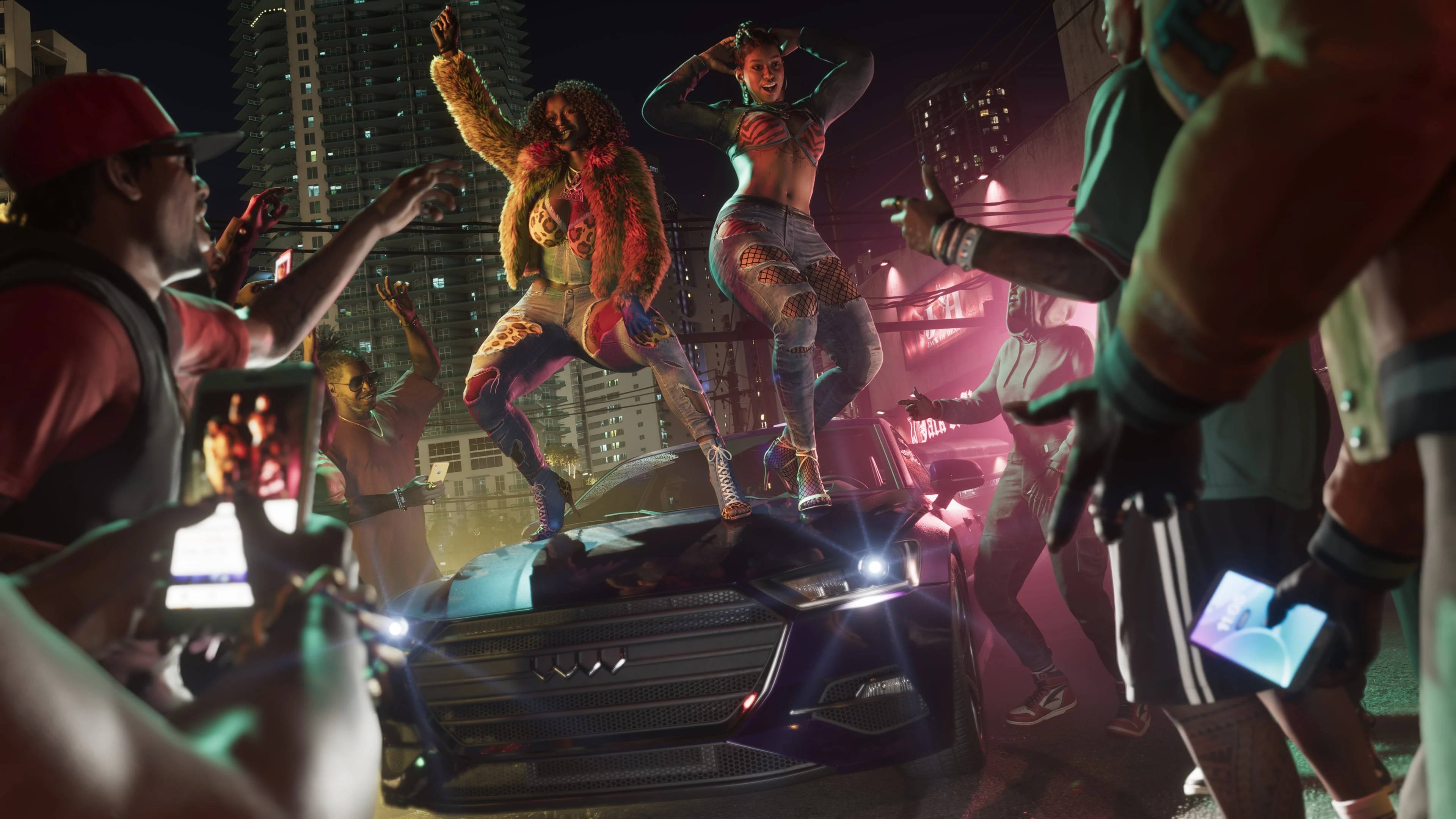 Two adult women dancing on a car while a nightlife crowd records them